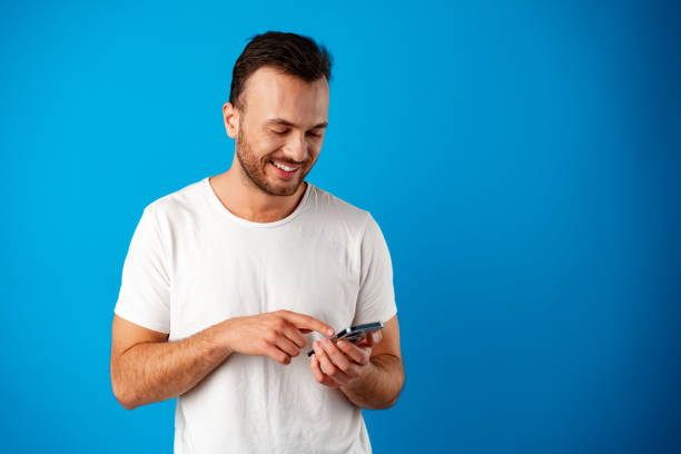 istock Man looking at phone, standing isolated on blue background 1356812327