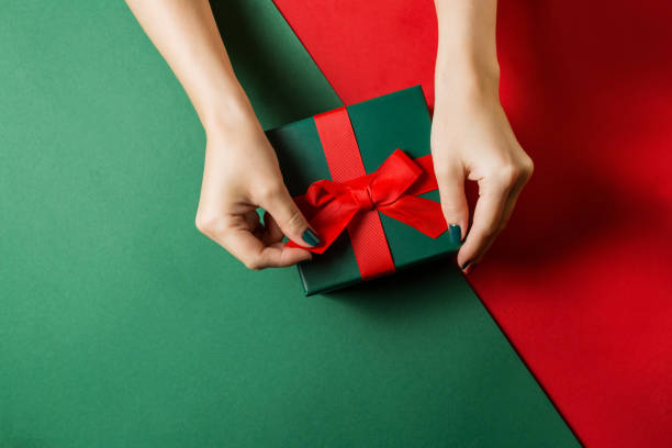 istock Hands with a colored manicure open a gift on a Christmas background 1356812369