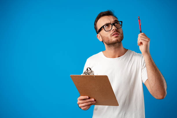 istock Portrait of young man making notes on clipboard against blue background 1356812600