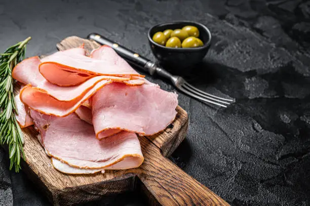 Photo of Pork ham slices on cutting board, Italian Prosciutto cotto. Black background. Top view. Copy space