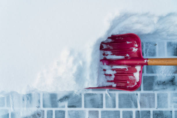 entfernung von schnee von pflasterplatten. es gibt eine rote schneeschaufel mit einem holzgriff. hintergrund. textur. - snow cleaning stock-fotos und bilder