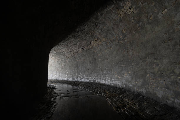 túnel de esgoto de alvenaria velho com luz da curva. rio subterrâneo ou velho coletor de água da chuva do século 19. - 19th hole - fotografias e filmes do acervo