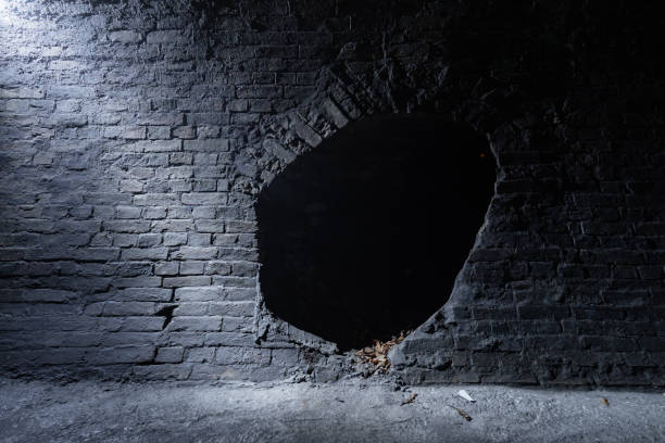 túnel de alvenaria escura seca de um antigo coletor de drenagem do século 19 com luz vindo da rua no canto superior esquerdo. parede de tijolos velha com um buraco no centro. - 19th hole - fotografias e filmes do acervo