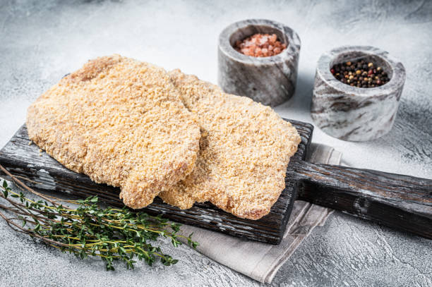 wiener raw schnitzel en pan rallado sobre tabla de madera. fondo blanco. vista superior - viennese schnitzel fotografías e imágenes de stock