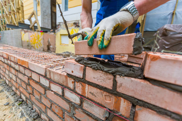 istock Bricklayer is near brickwork on exterior wall with putty knife in construction site. 1356832101