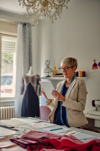 istock Senior fashion designer working in atelier and using tablet 1356833204