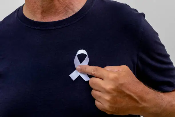 Photo of man putting white ribbon on his shirt. represents a mental health prevention program. January White.