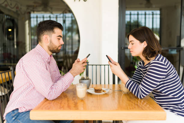Side view of a couple on a boring date Angry young woman and man feeling bored while dating at the coffee shop and texting on their smartphones communication problems stock pictures, royalty-free photos & images