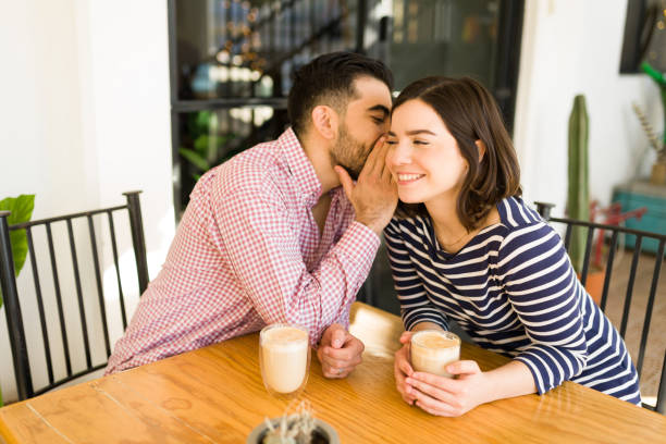 カフェでうわさ話をする若いカップル - whispering couple discussion smiling ストックフォトと画像