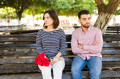 Angry couple having a misunderstanding. Caucasian man bringing flowers for her angry girlfriend at the park