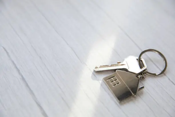 Photo of Silver key with silver house figure on white wooden background, buying new house real estate concept copy space