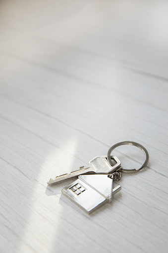Silver key with silver house figure on white wooden background, buying new house real estate concept copy space top view