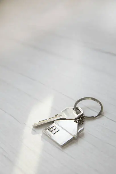 Photo of Silver key with silver house figure on white wooden background, buying new house real estate concept copy space