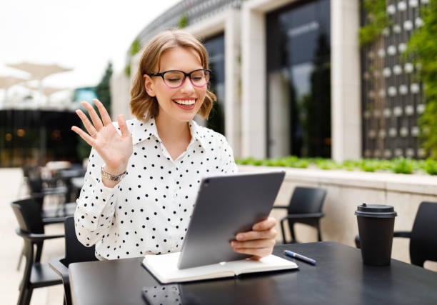 istock Positive woman tutor waving hello at webcam on digital tablet while giving online lesson outside 1356844066