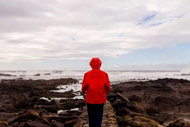 Woman wearing a red raincoat looking at the agitated sea