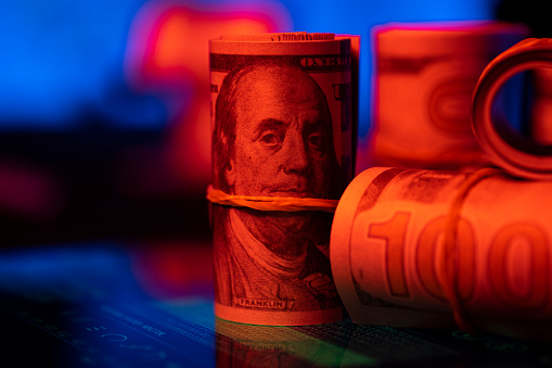 Bundles of hundred US dollar bills, under red and blue light.
