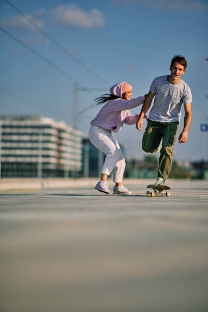 adolescentes brincalhões brincando. um garoto andando de skate enquanto uma garota o empurrava. - skateboarding skateboard teenager extreme sports - fotografias e filmes do acervo