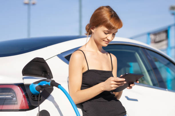 istock Girl working on tablet while her electric car is charging. 1356866899