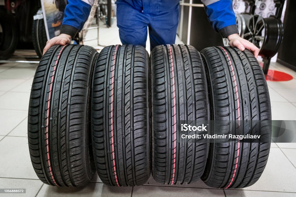 four new tires set of wheels demonstrates a new purchase by the seller, a wide gesture with his hands, tires close-up in the store four new tires set of wheels demonstrates a new purchase by the seller, a wide gesture with his hands, tires close-up in the store. Tire - Vehicle Part Stock Photo