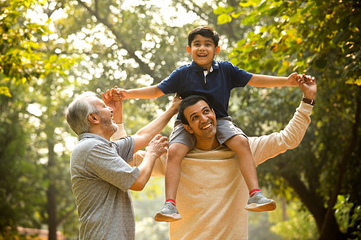 Grandfather having fun with boy enjoying sitting on father's shoulder at park