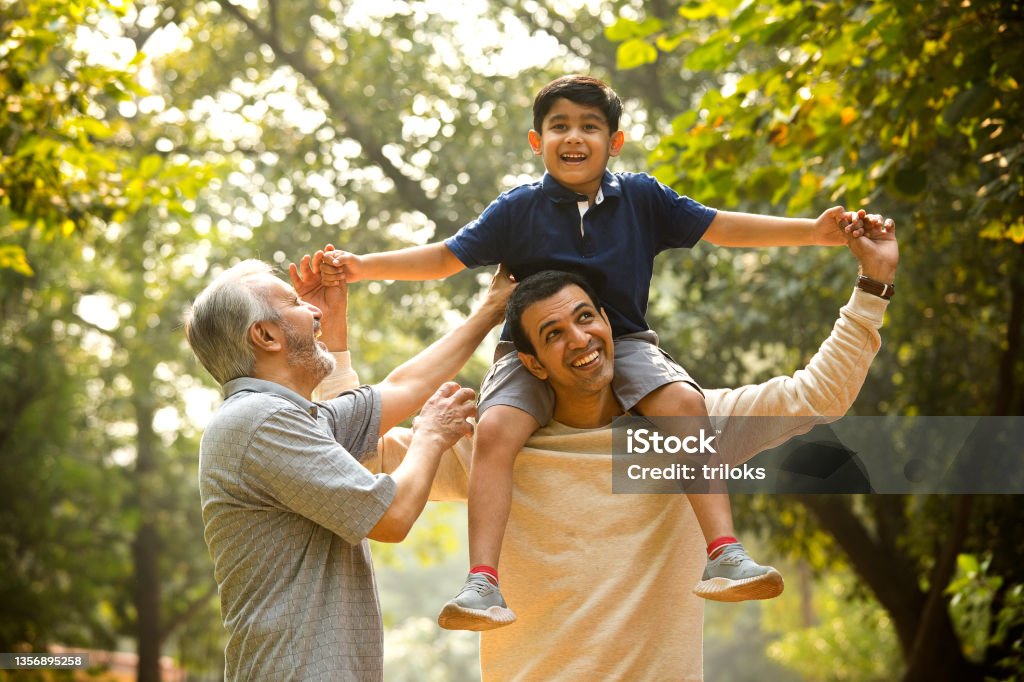Three generation family having fun at park Grandfather having fun with boy enjoying sitting on father's shoulder at park Family Stock Photo
