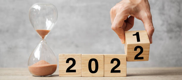 istock hand flipping block 2021 to 2022 text with hourglass on table. Resolution, time, plan, goal, motivation, reboot, countdown  and New Year holiday concepts 1356895749