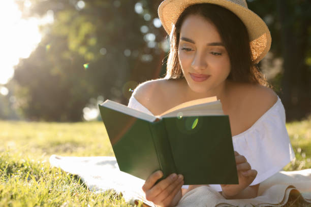 istock Beautiful young woman reading book in park 1356899870