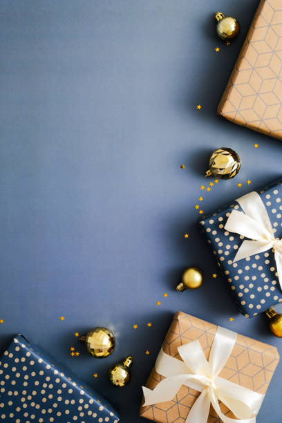 istock Christmas vertical blue background with gift boxes and gold Xmas baubles. Flat lay, top view, copy space. 1356907392