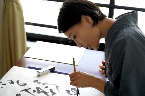 Japanese calligraphy set - Japanese woman in Kimono writing a character with a brush