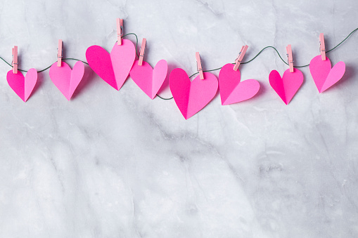 Pink paper cut hearts hanging on a clothesline with wooden clothespins. Space for copy.