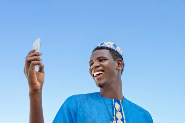 istock Young man using his mobile phone under a blue sky, traditional clothing, photo 1356908304