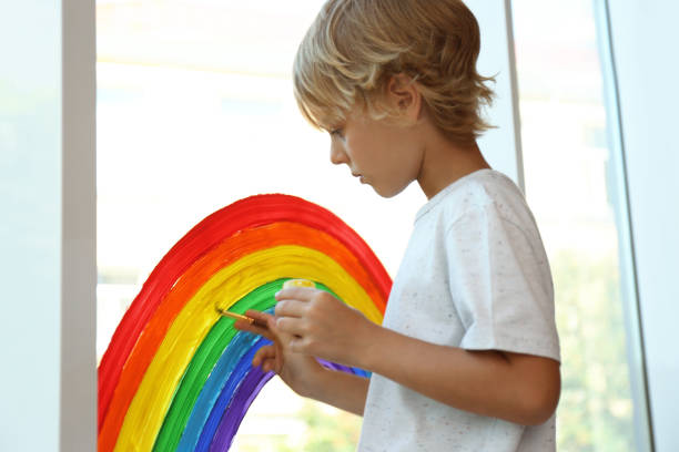 istock Little boy drawing rainbow on window. Stay at home concept 1356908380