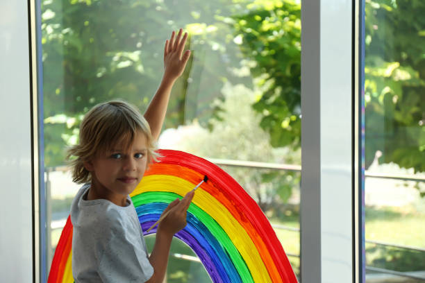 istock Little boy drawing rainbow on window. Stay at home concept 1356908422