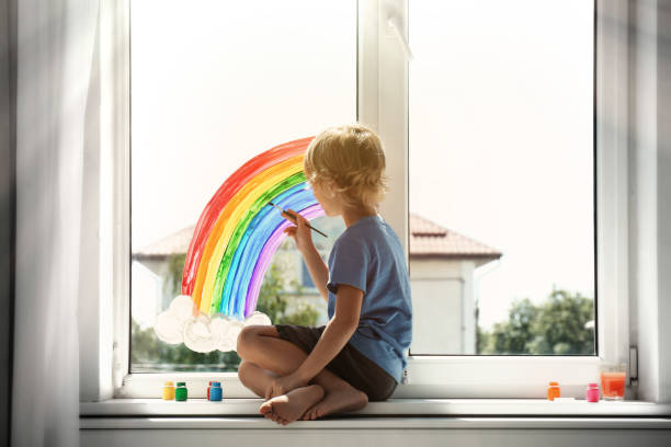 little boy drawing rainbow on window indoors. stay at home concept - primary care imagens e fotografias de stock