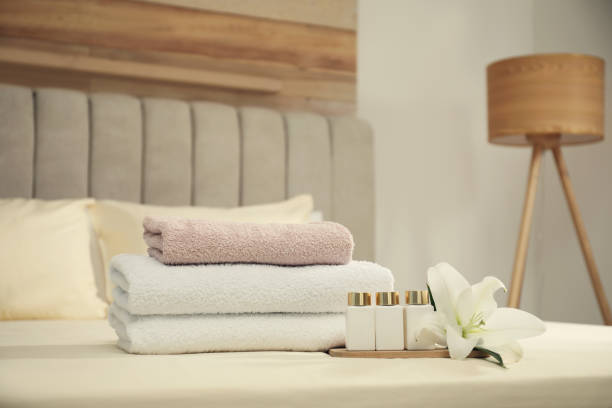 istock Stack of clean towels, flower and shampoo bottles on bed indoors. Space for text 1356910610