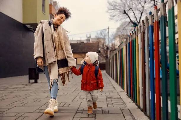 Babysitter taking kindergarten boy in kindergarten. Babysitter holding hands with little boy and taking him to kindergarten.