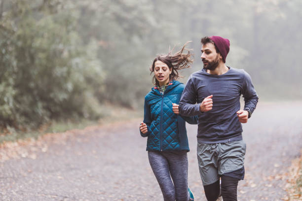 istock Young athletic couple running during cold day in misty forest. 1356914441