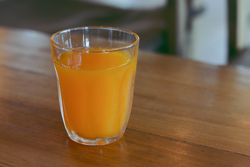 Glass of orange juice on wooden table.