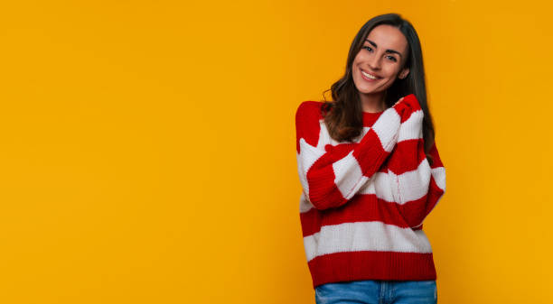 istock Charming happy beautiful smiling young woman in striped sweater while she posing, looking on camera and isolated on yellow background 1356916855