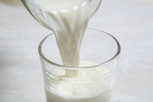 istock Pouring milk into glass on white table, closeup 1356917457
