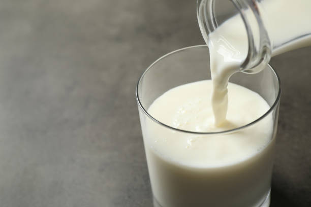 istock Pouring milk into glass on grey table, closeup. Space for text 1356917646