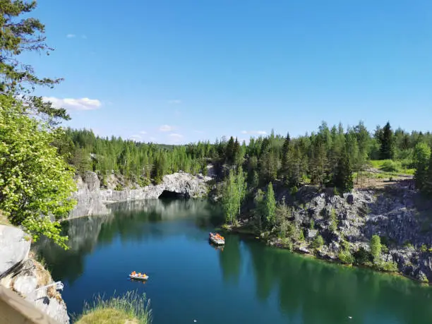 Photo of View from the observation deck of the turquoise water of the Marble Canyon in the Ruskeala Mountain Park with the reflection of the sky and trees on a sunny summer day.