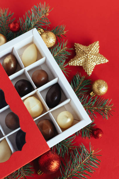istock Gift box with chocolate candies, spruce branches, red and golden balls on a red background. Holiday concept. 1356919087