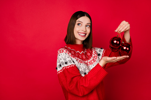 Photo of shiny adorable young lady wear print sweater holding balls looking back empty space isolated red color background.