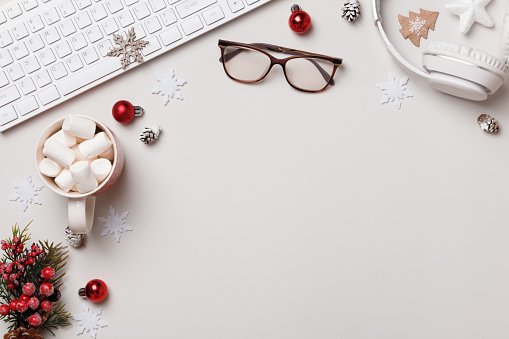 Winter desktop. New Year Christmas composition. Keyboard glasses gift marshmallow headphones on the gray table. Flat lay top view