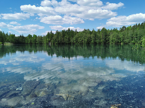 The shore of the lake is bright with clear water, in which you can see the marble on the bottom and reflect the sky with clouds, in the mountain park Ruskeala.