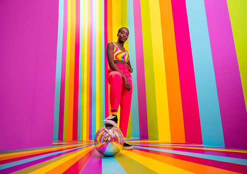 Beautiful african american young woman dancer having fun inside a rainbow box room - Cool and stylish afro adult woman portrait on multicolored background, influencer creating content for social networks in a selfie room