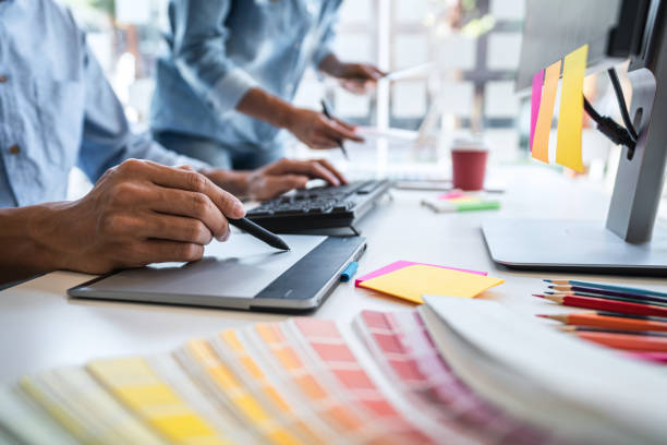 istock Two colleague creative graphic designer working on color selection and color swatches, drawing on graphics tablet at workplace with work tools and accessories 1356923721