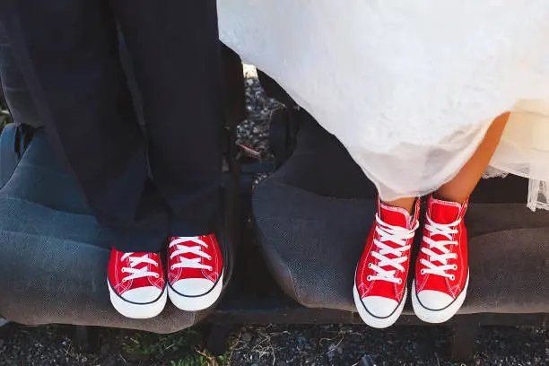 Photo of The bride and groom in red sneakers in the junkyard car