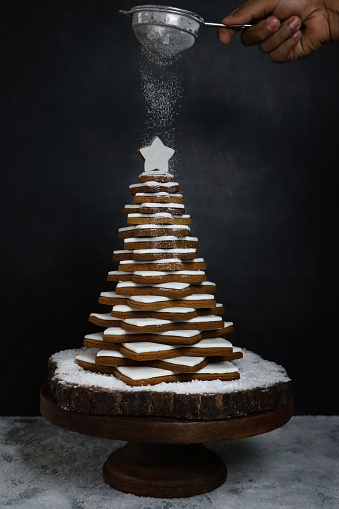 Stock photo showing close-up view of stack of star shaped gingerbread biscuits decorated with white royal icing forming a Christmas tree. Home baking concept.